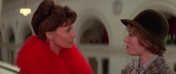 Movie still from “Damien: Omen II” (1978), directed by Mike Hodges – A woman in a red jacket and a man in a brown hat; Close Up shot, Over the shoulder angle