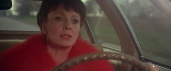 Movie still from “Damien: Omen II” (1978), directed by Mike Hodges – An older woman in a red coat driving a car; Close Up shot, Over the shoulder angle