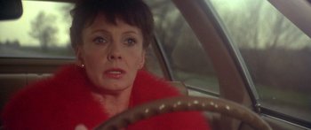 Movie still from “Damien: Omen II” (1978), directed by Mike Hodges – A woman wearing a red coat driving a car; Close Up shot, Over the shoulder angle