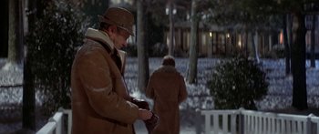 Movie still from “Damien: Omen II” (1978), directed by Mike Hodges – A man in a brown coat and a brown hat is looking at his phone; Medium shot, Over the shoulder angle