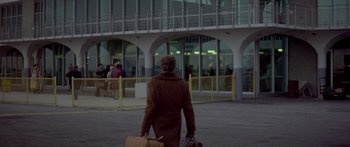 Movie still from “Damien: Omen II” (1978), directed by Mike Hodges – An older woman is walking with her luggage in her hand; Extreme Wide shot, High angle