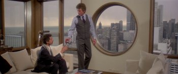 Movie still from “Damien: Omen II” (1978), directed by Mike Hodges – A man standing in front of another man in front of a large window; Wide shot, Over the shoulder angle