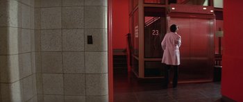 Movie still from “Damien: Omen II” (1978), directed by Mike Hodges – A woman in a white lab coat walks through a hallway; Wide shot, Over the shoulder angle