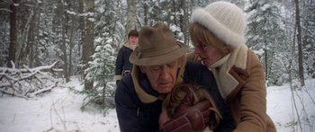 Movie still from “Damien: Omen II” (1978), directed by Mike Hodges – An older man holding a young child in a snowy forest; Medium shot, Low angle
