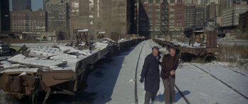 Movie still from “Damien: Omen II” (1978), directed by Mike Hodges – Two people standing on a snowy street next to a train track; Wide shot, High angle