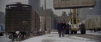 Movie still from “Damien: Omen II” (1978), directed by Mike Hodges – Two people walking down a snow covered sidewalk; Extreme Wide shot, High angle