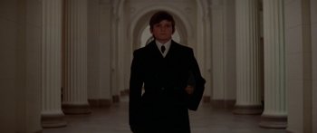 Movie still from “Damien: Omen II” (1978), directed by Mike Hodges – A man in a suit and tie standing in a hallway; Medium shot, Low angle