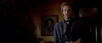 Movie still from “Dances with Wolves” (1990), directed by Kevin Costner – A man in a uniform standing in front of a painting; Close Up shot, Over the shoulder angle