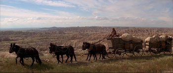 Movie still from “Dances with Wolves” (1990), directed by Kevin Costner – A man riding on the back of a horse drawn carriage; Extreme Wide shot, Low angle