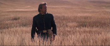 Movie still from “Dances with Wolves” (1990), directed by Kevin Costner – A man standing in a field holding a gun; Medium shot, Low angle