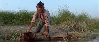 Movie still from “Dances with Wolves” (1990), directed by Kevin Costner – A man wearing a hat and holding a bucket on top of a wooden platform; Medium shot, Low angle