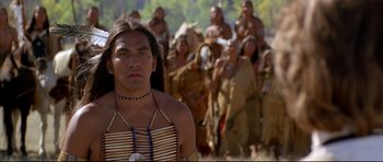 Movie still from “Dances with Wolves” (1990), directed by Kevin Costner – A man in a native american outfit standing in front of a group of people; Close Up shot, Over the shoulder angle