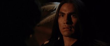 Movie still from “Dances with Wolves” (1990), directed by Kevin Costner – A man with long black hair wearing a black shirt and a feather; Close Up shot, Over the shoulder angle