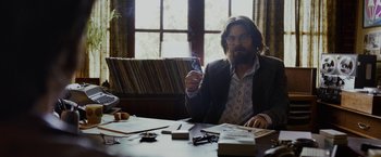 Movie still from “Danny Collins” (2015), directed by Dan Fogelman – A man sitting at a table smoking a cigarette; Medium shot, Over the shoulder angle
