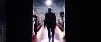 Movie still from “Danny Collins” (2015), directed by Dan Fogelman – A man in a suit walks down the aisle of an event; Wide shot, Low angle