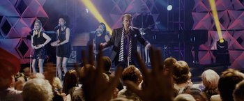 Movie still from “Danny Collins” (2015), directed by Dan Fogelman – A man singing into a microphone in front of an audience; Wide shot, High angle