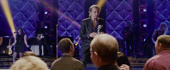Movie still from “Danny Collins” (2015), directed by Dan Fogelman – A man in a black jacket is speaking to a crowd; Medium shot, Over the shoulder angle