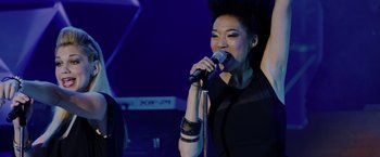 Movie still from “Danny Collins” (2015), directed by Dan Fogelman – A woman is singing into a microphone on a stage; Medium shot, Overhead angle