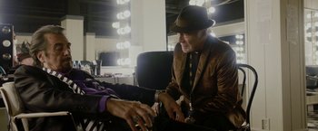 Movie still from “Danny Collins” (2015), directed by Dan Fogelman – A man wearing a brown jacket and a brown hat is talking to another man in front of a mirror; Medium shot, Over the shoulder angle