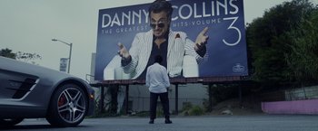 Movie still from “Danny Collins” (2015), directed by Dan Fogelman – A man standing in front of a large billboard; Wide shot, Over the shoulder angle
