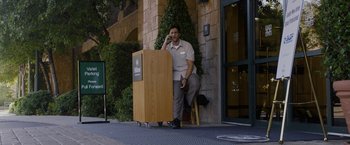 Movie still from “Danny Collins” (2015), directed by Dan Fogelman – A man standing next to a podium on a cell phone; Wide shot, High angle