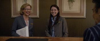 Movie still from “Danny Collins” (2015), directed by Dan Fogelman – A woman standing next to a man at a desk; Medium shot, Low angle