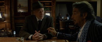 Movie still from “Danny Collins” (2015), directed by Dan Fogelman – An older man wearing a suit and a hat is sitting at a table; Medium shot, Over the shoulder angle