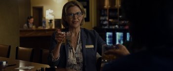 Movie still from “Danny Collins” (2015), directed by Dan Fogelman – A woman sitting at a table holding a drink; Medium shot, Over the shoulder angle
