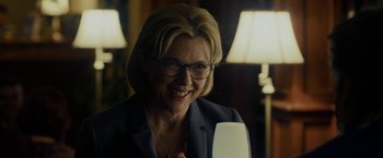 Movie still from “Danny Collins” (2015), directed by Dan Fogelman – A woman wearing glasses and a suit smiling; Close Up shot, Over the shoulder angle