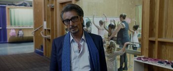 Movie still from “Danny Collins” (2015), directed by Dan Fogelman – A man in a suit and tie standing in front of a group of people; Medium shot, Over the shoulder angle