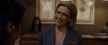 Movie still from “Danny Collins” (2015), directed by Dan Fogelman – A woman wearing glasses and a suit smiling; Close Up shot, Over the shoulder angle