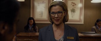 Movie still from “Danny Collins” (2015), directed by Dan Fogelman – A woman wearing glasses standing in front of a counter; Close Up shot, Over the shoulder angle