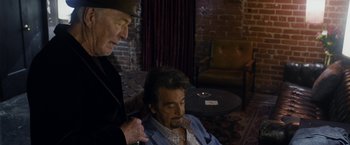 Movie still from “Danny Collins” (2015), directed by Dan Fogelman – A man sitting in front of another man in front of a brick wall; Medium shot, Over the shoulder angle