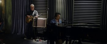 Movie still from “Danny Collins” (2015), directed by Dan Fogelman – A man sitting in front of a piano next to another man playing a guitar; Wide shot, High angle