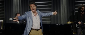 Movie still from “Danny Collins” (2015), directed by Dan Fogelman – A man in a jacket and tie pointing to the side; Medium shot, Over the shoulder angle
