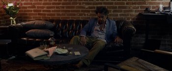 Movie still from “Danny Collins” (2015), directed by Dan Fogelman – A man sitting on top of a black leather couch; Medium shot, High angle