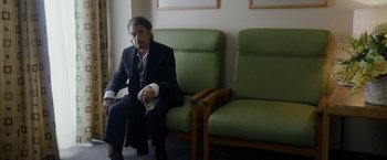 Movie still from “Danny Collins” (2015), directed by Dan Fogelman – A man sitting on a couch in a room; Medium shot, Over the shoulder angle