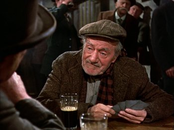 Movie still from “Darby O'Gill and the Little People” (1959), directed by Robert Stevenson – An older man sitting at a table with a glass of beer; Medium shot, Over the shoulder angle