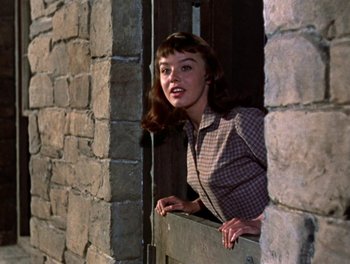 Movie still from “Darby O'Gill and the Little People” (1959), directed by Robert Stevenson – A woman leaning up against a brick wall; Medium shot, Low angle