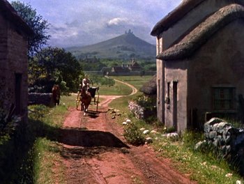 Movie still from “Darby O'Gill and the Little People” (1959), directed by Robert Stevenson – A horse drawn carriage traveling down a dirt road near a house; Extreme Wide shot, High angle