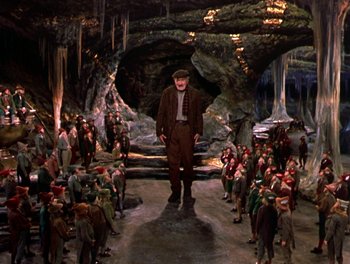 Movie still from “Darby O'Gill and the Little People” (1959), directed by Robert Stevenson – A man in a suit and hat standing in front of a group of people; Wide shot, High angle