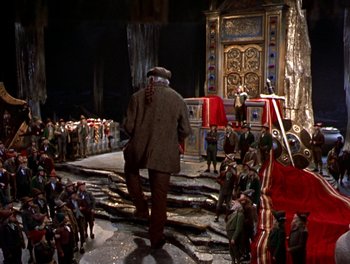 Movie still from “Darby O'Gill and the Little People” (1959), directed by Robert Stevenson – A man in a coat and hat walks down stairs in front of a crowd; Wide shot, High angle