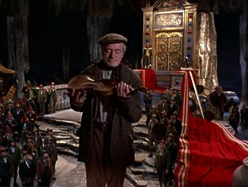 Movie still from “Darby O'Gill and the Little People” (1959), directed by Robert Stevenson – An old man is holding an instrument while standing in front of a crowd of people; Wide shot, High angle