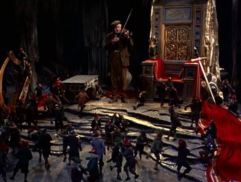 Movie still from “Darby O'Gill and the Little People” (1959), directed by Robert Stevenson – A group of people in a room with a man playing a fiddler; Extreme Wide shot, High angle