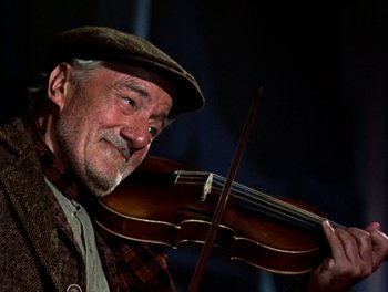 Movie still from “Darby O'Gill and the Little People” (1959), directed by Robert Stevenson – An older man holding a violin in his hands; Close Up shot, Low angle