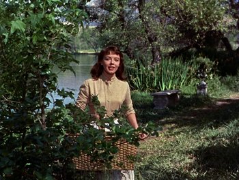 Movie still from “Darby O'Gill and the Little People” (1959), directed by Robert Stevenson – A woman holding a basket near a body of water; Medium shot, Over the shoulder angle
