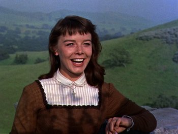 Movie still from “Darby O'Gill and the Little People” (1959), directed by Robert Stevenson – A young woman smiles brightly while standing in front of a hill; Close Up shot, Low angle