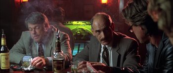 Movie still from “Dark Blue” (2002), directed by Ron Shelton – An older man sitting at a table in front of a bottle of alcohol; Medium shot, Low angle