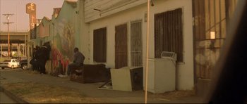 Movie still from “Dark Blue” (2002), directed by Ron Shelton – A man sitting on the ground outside of a building; Wide shot, Low angle