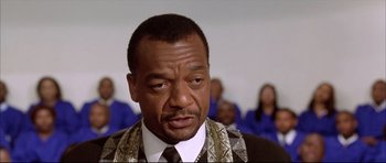 Movie still from “Dark Blue” (2002), directed by Ron Shelton – A man in a suit and tie with a group of people in the background; Close Up shot, Low angle